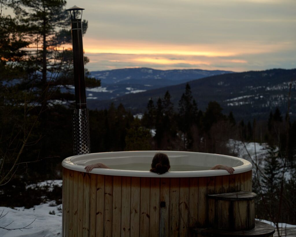 Wooden outdoor hot tub on a snowy terrace looking over mountains at sunset